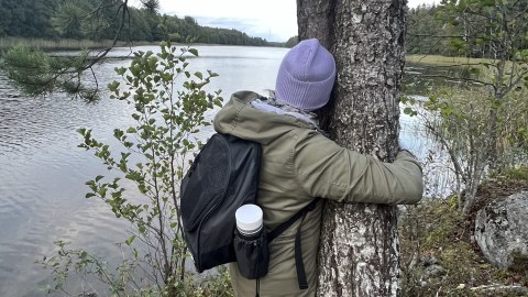 Woman hugging a tree by a Finnish lake
