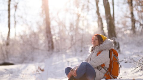 Nainen istuu metsässä talvisella auringonpaisteella