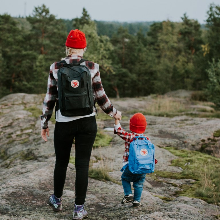 Äiti ja lapsi kävelevät käsi kädessä metsäisellä kalliolla.