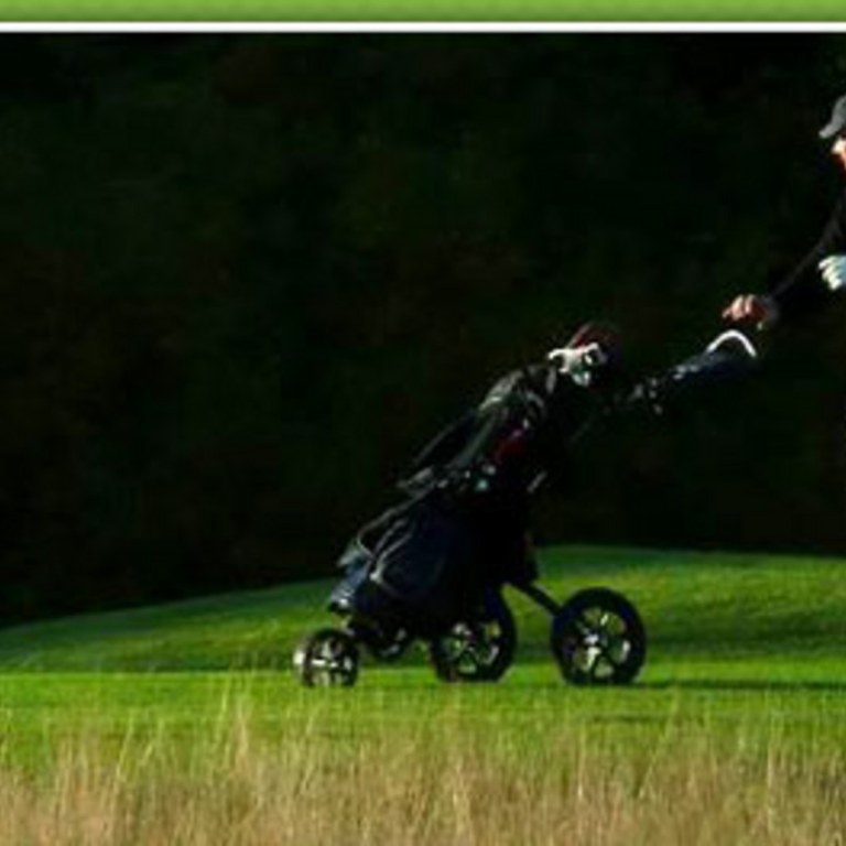 Golfaaja työntää golfkärryjä kentällä.