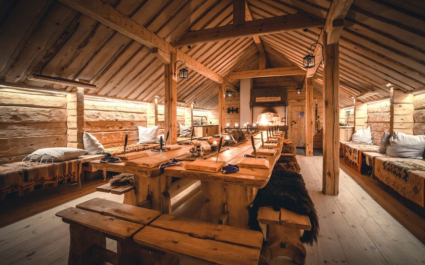 The hall of the Wäinölä log building with a long wooden table and long benches. The table is set.