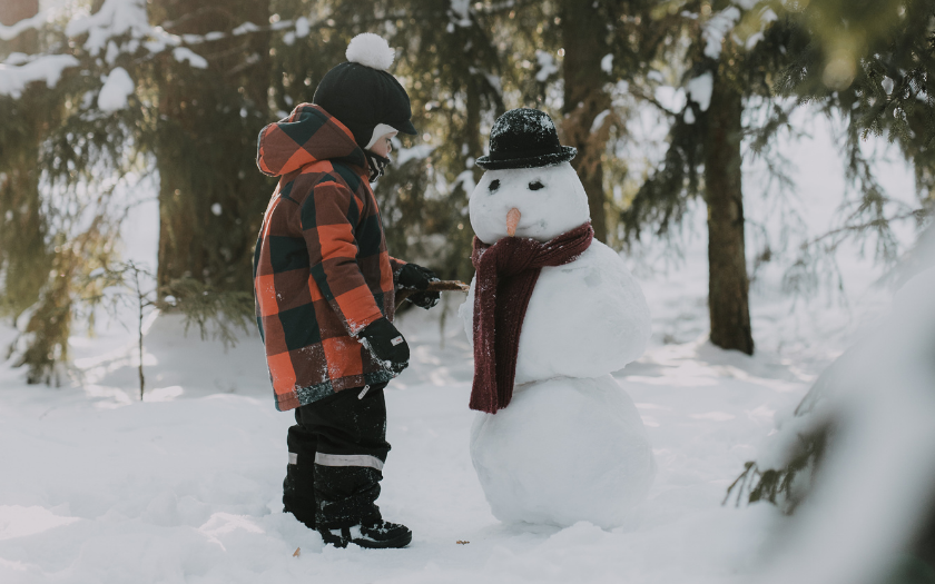 Child standing next to snowman