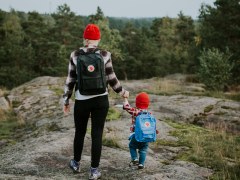 Äiti ja lapsi kävelevät käsi kädessä metsäisellä kalliolla.