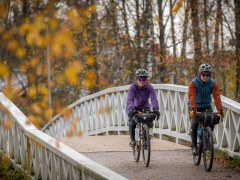 Kaksi pyöräilijää tunnelmallisella sillalla ympärillään ruskan värit.