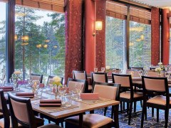 Ravintolasali, jonka pöysissä juhlakattaus. Pöytien takana isot ikkunat, joista avautuu luminen metsämaisema.