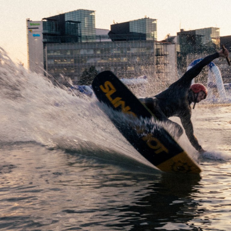 A person wakeboarding in the sea. Tall buildings on the beach behind.
