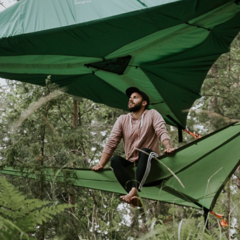 Henkilö istumassa puussa roikkuvan Tentsile-teltan alakankaalla/-tasolla.