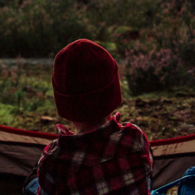 A child with her/his back to the camera in the tent's doorway looking at the forest landscape.