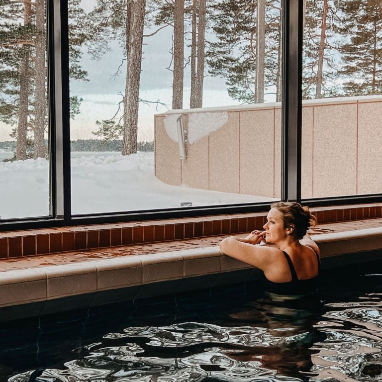 Woman in indoor pool looking on outdoor nature