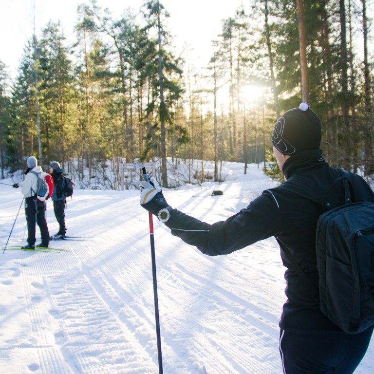 Kolme hiihtäjää aurinkoisessa talvisäässä ladun varressa.