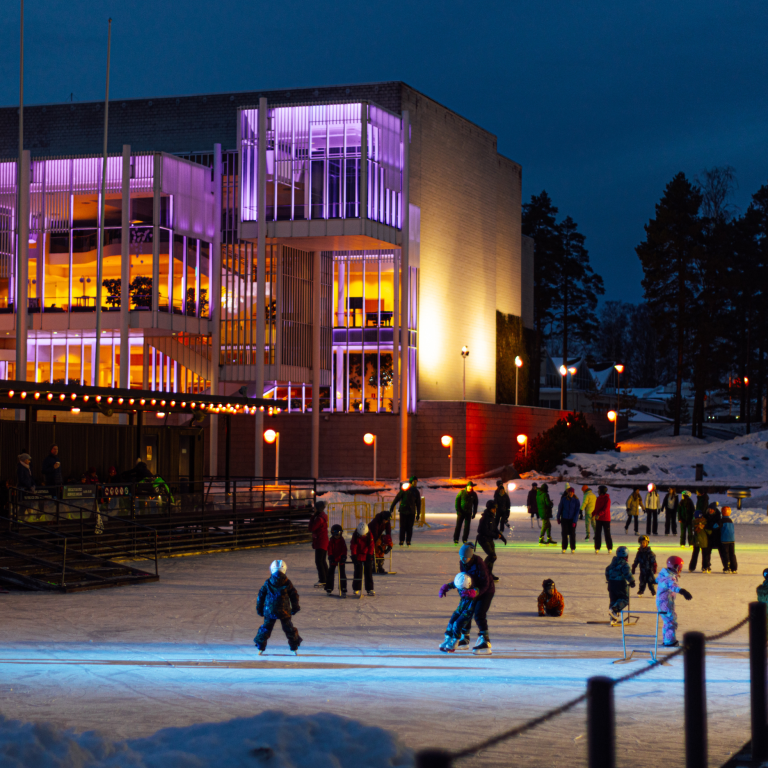After dark people ice skating at artificial ring Tapiola Ice Garden with building of Finnish Cultural Centre right behind