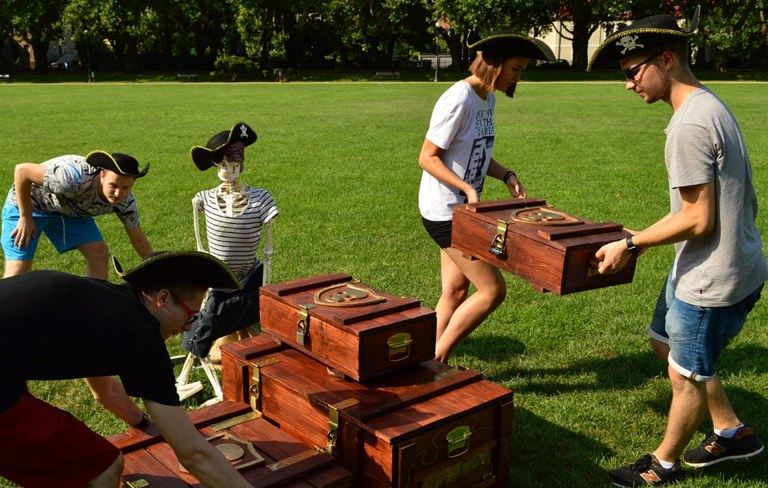 Four people solving a treasure chest puzzle in an escape game outdoors.