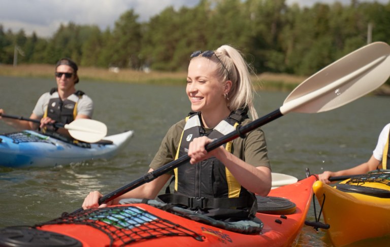 A smiling  woman and a man kayaking in the archipelago of Espoo