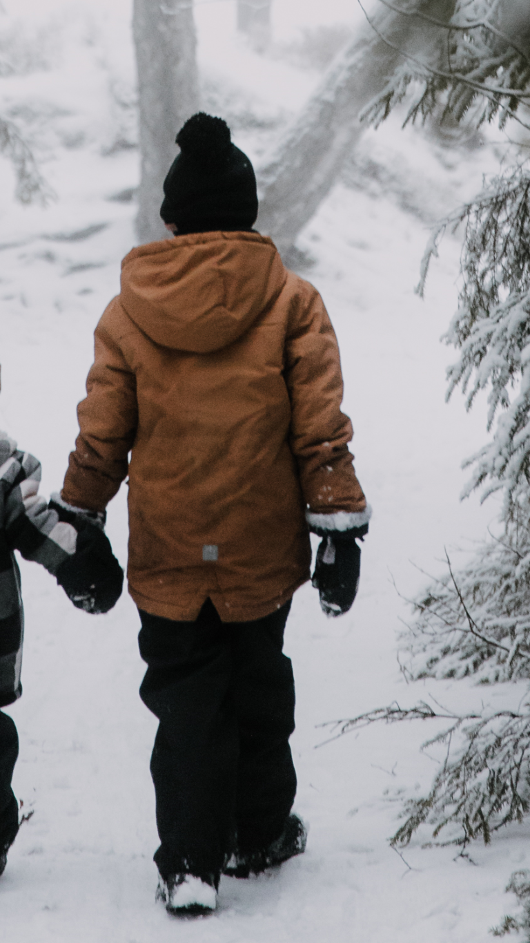 Lapset kävelevät käsi kädessä lumisessa metsässä.