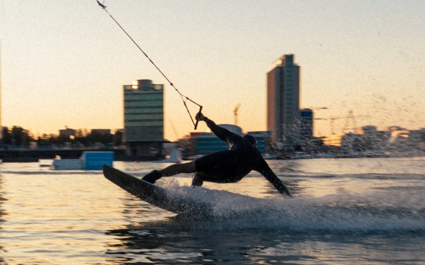 A person wakeboarding in the sea. Tall buildings on the beach behind.