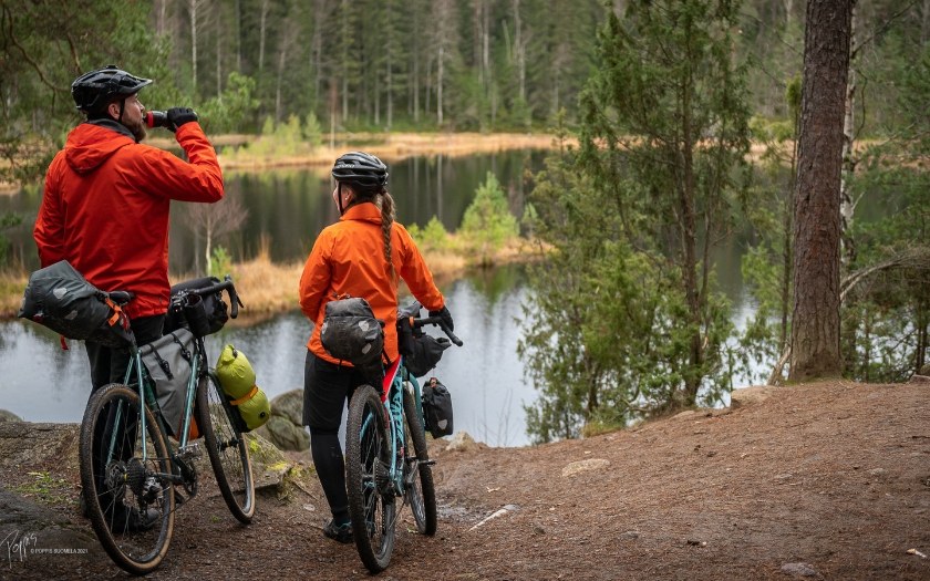 Two cyclists standing and snacking by the lake in forest