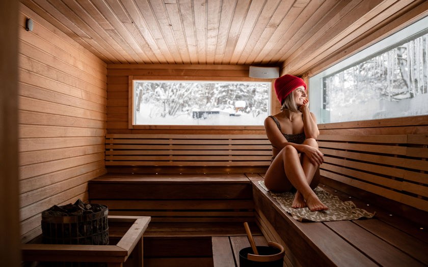 Nainen istuu pipo päässä saunan lauteilla Löyöykontissa katsellen ulos talvista maisemaa.
