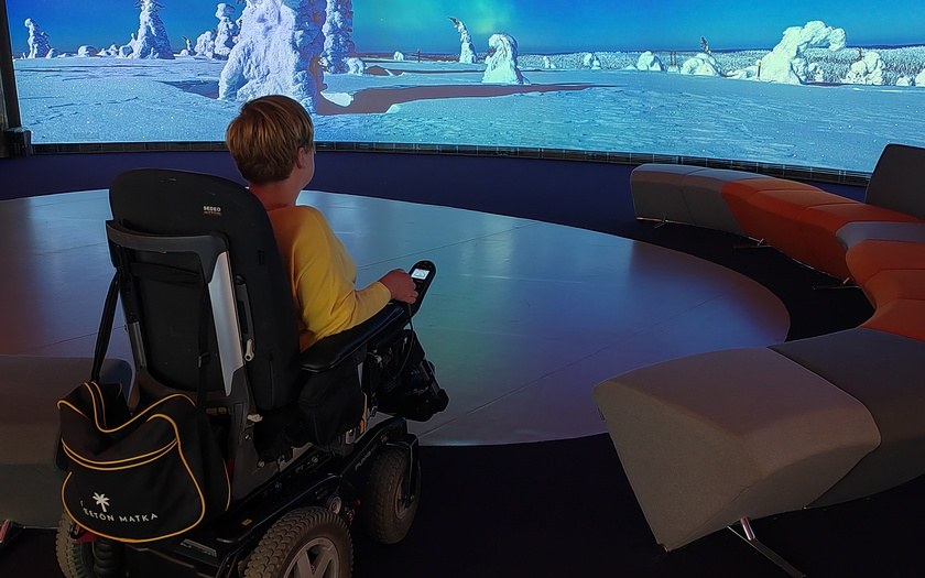  Ihminen sähköpyörätuolilla katsomassa Suomen luontokeskus Haltian näyttelyseinää.