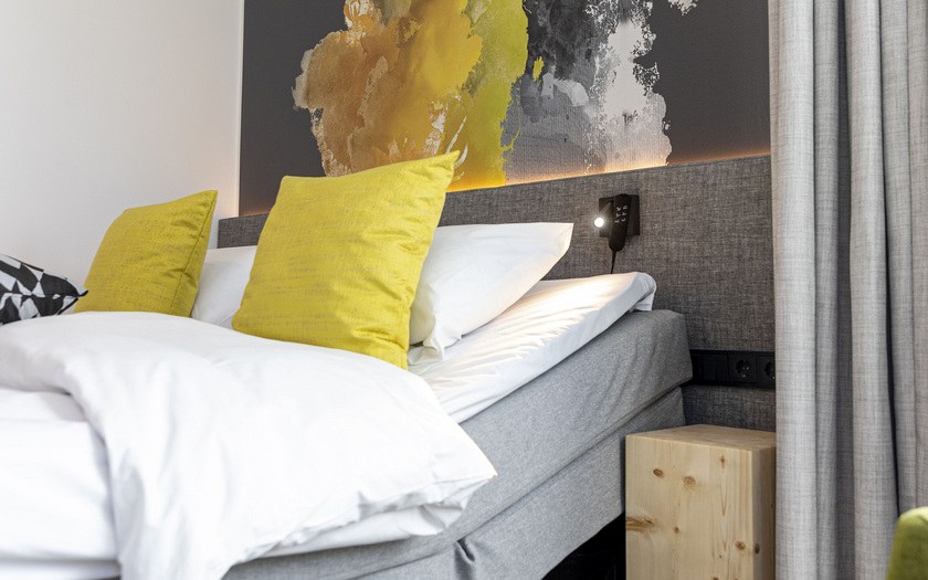 Kuva hotelli GLO Espoon huoneesta ja motorisoidusta sängystä, jonka taustalla on taideteos seinällä.