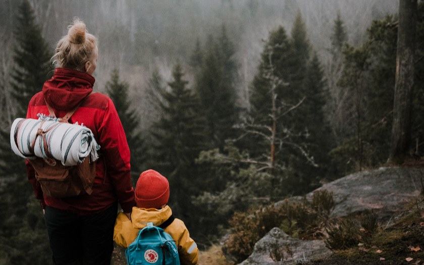 Äiti ja lapsi kukkulan päällä seisomassa käsi kädessä utuisessa Nuuksion metsämaisemassa.