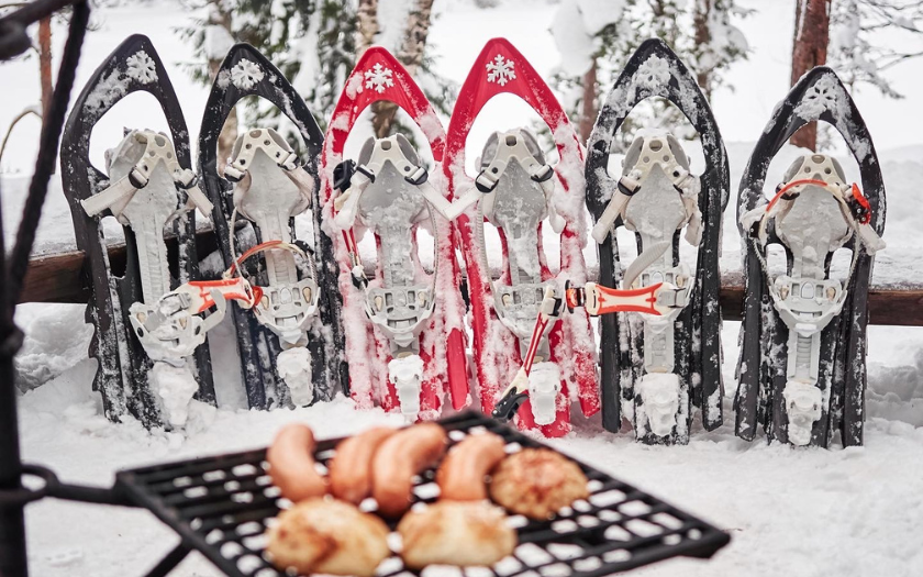 Snowshoes in a row and campfire with sausages on snow