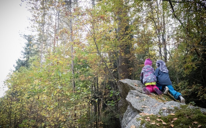 Kaksi lasta tarkkailee metsää kalliolta käsin.