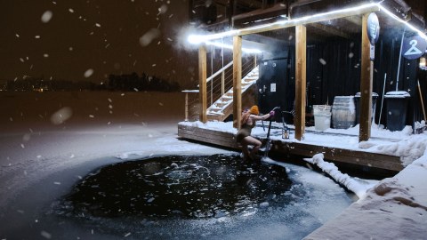 Woman dipping into ice cold water in front of Laguuni floating sauna