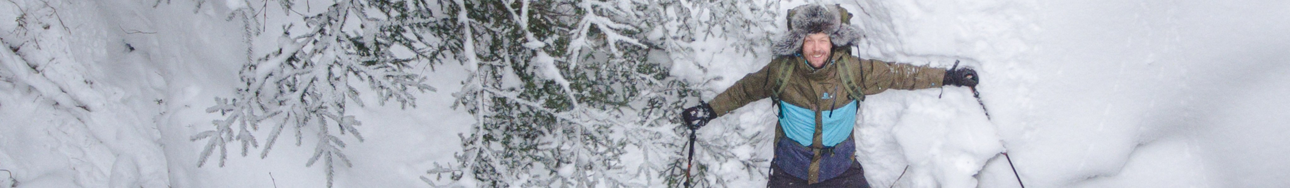 Mies makaa lumessa metsässä talvivarusteissa ja lumikengissä.