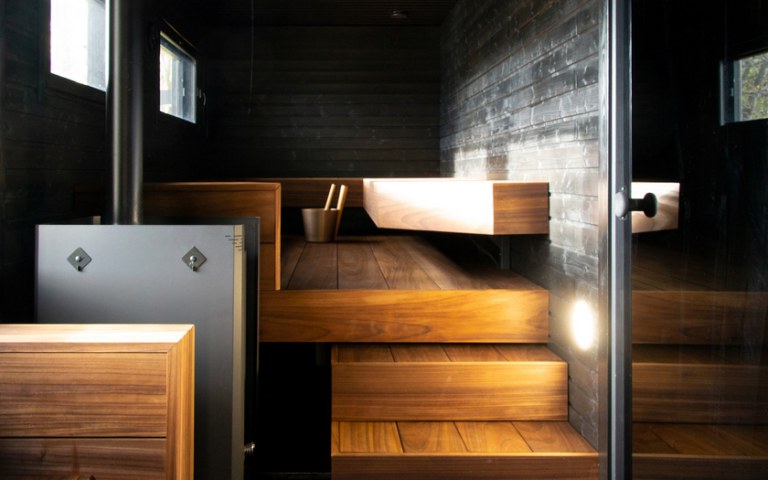 Tummansävyinen sauna, jonka lauteilla kiulu.